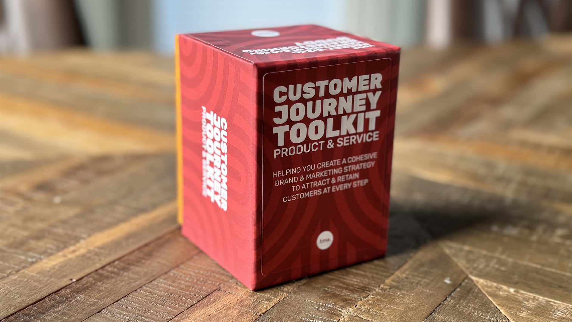 A red box labeled "Customer Journey Toolkit: Product & Service" sits on a wooden table, promoting a cohesive brand and marketing strategy to retain customers.