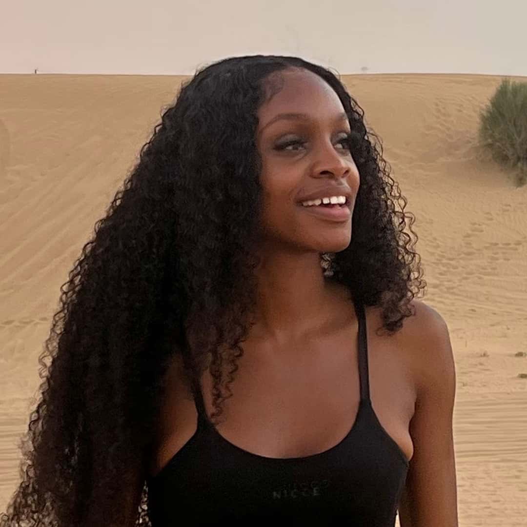 A woman with long curly hair wearing a black tank top stands smiling in a desert landscape, embodying the essence of Famo.