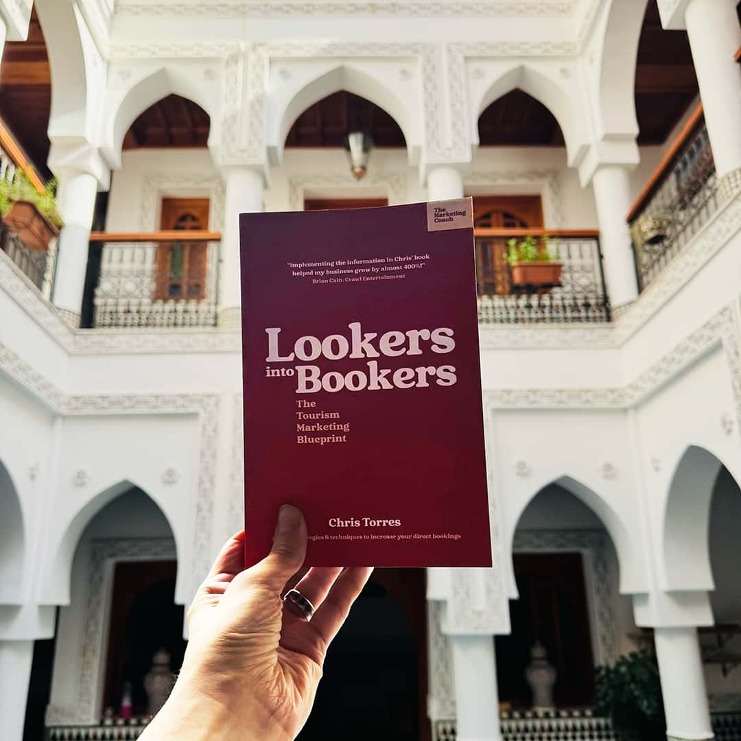 In an intricate architectural courtyard, a person proudly holds "Lookers into Bookers" by Chris Torres, showcasing the transformative power of its insights.